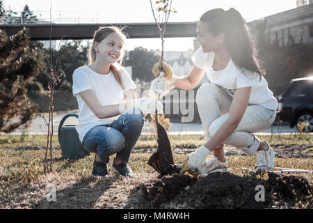 Freundliche hübsche Mädchen helfen, einen Baum zu pflanzen, Stockfoto