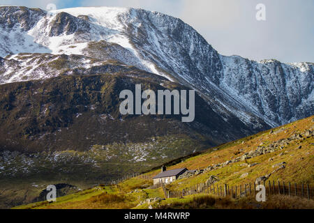 Wild walisische Landschaft im Winter mit Sonne über einem alten Bauernhaus in der Cwm Eigiau oder Eigau Tal mit schneebedeckten Penybonc Eryl Farchog Stockfoto
