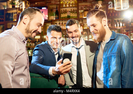 Gruppe von Fröhlichen Freunden unter selfie mit Hilfe von Smartphones zusammen im Pub nach einem harten Arbeitstag gesammelt Stockfoto