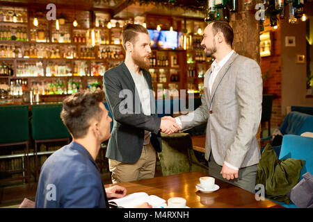 Junge Unternehmer in formale zitternden Hand Bärtigen von seinem Partner nach dem erfolgreichen Abschluss der Verhandlungen in modernes Cafe, Assistant ma Stockfoto