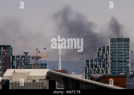 London, Großbritannien. 18 Feb, 2018. London Brand: Schwarzer Rauch steigt über Gebäude aus East London mit Emirates Airline Seilbahnen im Blick. Credit: Guy Corbishley/Alamy leben Nachrichten Stockfoto