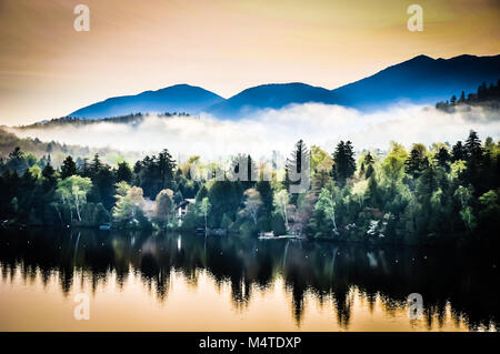 Reflexionen der Adirondack Mountains und am frühen Morgen Dunst und Nebel auf Mirror Lake in Lake Placid, New York. Stockfoto