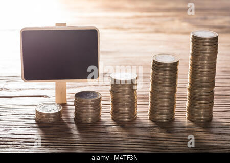 Leere kleine Kreidetafel Mit zunehmender Coin Stack auf hölzernen Tisch Stockfoto