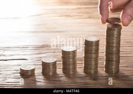 Nahaufnahme einer Person, eine Münze auf zunehmende Münze Stapel über die hölzerne Tabelle Stockfoto