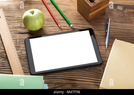 Grüner Apfel und leerer Bildschirm digitale Tablette auf Holztisch mit Büromaterial Stockfoto