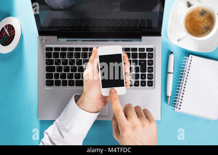 Erhöhten Blick auf ein Geschäftsmann mit Mobiltelefon mit dem offenen Laptop Stockfoto