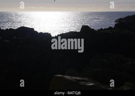 Glitzernde blaue Nordsee über Silhouetted zerklüfteten Granitfelsen. Neue Slains Castle, Cruden Bay, Aberdeenshire, Schottland, Großbritannien. Stockfoto