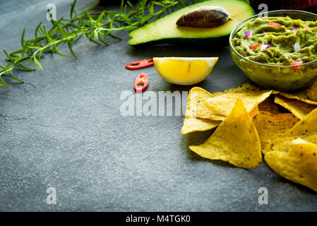Guacamole Schüssel mit Zutaten und Tortilla Chips auf einem Tisch aus Stein. Selektive konzentrieren. Copyspace für Ihren Text. Stockfoto