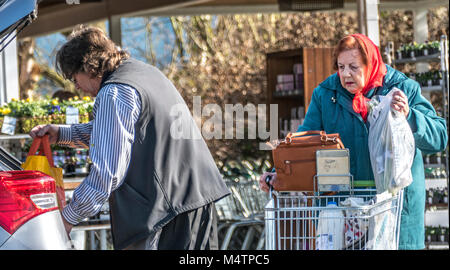 Männliche Waitrose Supermarkt Mitarbeiter und helfen, eine alte/ältere Frau mit ihrem Shopping auf der Rückseite in Ihr Auto, am Ruislip Zweig, England, UK. Stockfoto