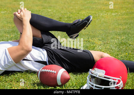 Nahaufnahme der Verletzten American Football Player liegen auf Feld mit Rugby und Helm. Stockfoto