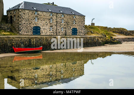 Kleine rote Ruderboot, malerischen Hafen, Portsoy, Aberdeenshire, Schottland, Großbritannien, mit Wasser Reflexion, historischen Gebäuden dolphin Skulptur Stockfoto