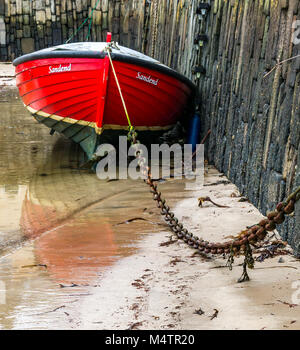 Nahaufnahme von verketteten Kleine rote Boot bei Ebbe von Sandend, malerischen Hafen, Portsoy, Aberdeenshire, Schottland, Großbritannien, mit Wasser Reflexionen Stockfoto