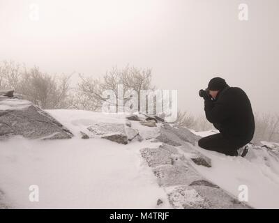 Fotograf nimmt Bild von Freeze herbstliche Tagesanbruch, Felsen, bedeckt mit frischem Pulverschnee. Stony Rock Peak aus dicken Nebel erhöht. Stockfoto