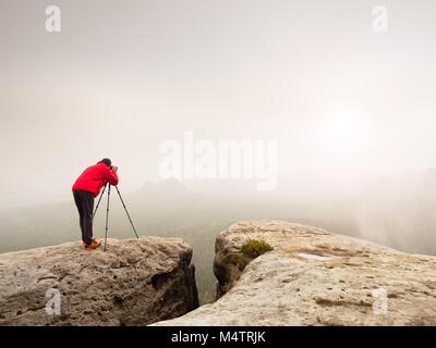 Professionelle Fotografen schießen. Artist Aufenthalt mit Stativ auf dem Gipfel und nimmt Bilder der herbstlichen Coutryside. Misty Landschaft, kalten Sonnenaufgang in Fa Stockfoto