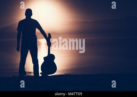 Gitarrist mit akustischer Gitarre Sonnenuntergang Silhouette Konzept Foto mit der rechten Seite kopieren. Stockfoto