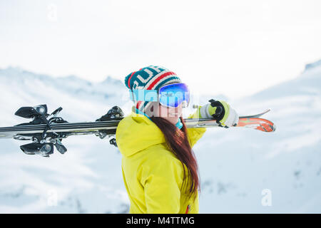 Seitenansicht der lächelnde Frau in der Maske mit Skiern auf der Schulter Stockfoto