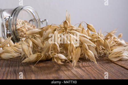 In der Nähe von trockenen Hafer auf vintage Holztisch. Schöne reife Mais mit Glas Glas voller Haferflocken im Hintergrund. Kleine Tiefe der Schärfe. Stockfoto