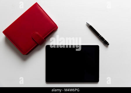 Business Office Elemente auf weißer Tisch, Tablet und roten Notizbuch mit Stift Stockfoto