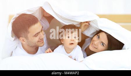 Glückliche Familie, die unter einer Bettdecke, während Sie an der Kamera Stockfoto