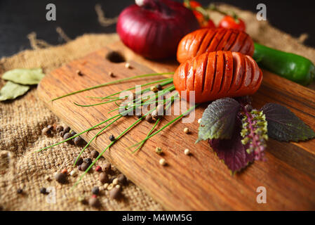 Gegrillte Würstchen auf einem Holzbrett mit Salat, Basilikum, Tomaten, Zwiebeln und Paprika. Stockfoto