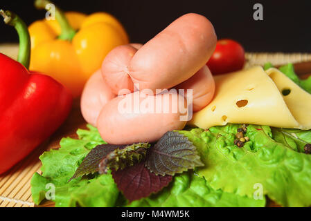 Würstchen mit Käse auf einem Holzbrett mit Salat, Basilikum, Tomaten und Paprika. Stockfoto