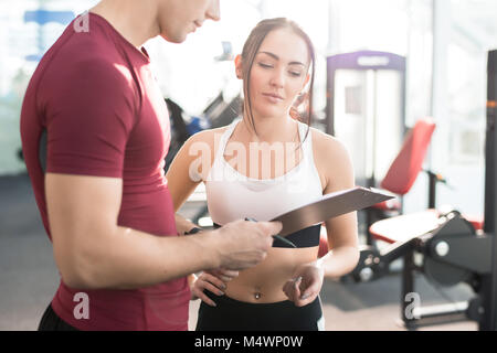Taille bis Porträt der jungen Frau unterzeichnen Vertrag mit Personal Fitness Trainer in der modernen Gym Club Stockfoto