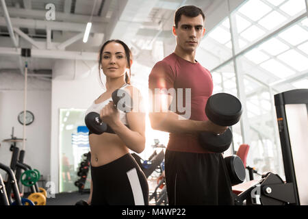 Taille bis Portrait von Fit sportliche Paar mit kurzhanteln an Kamera suchen im modernen Fitnessraum posing Stockfoto