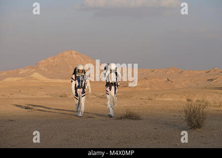 Analoge Astronauten, verkleidet in einem speziellen Raumanzügen, umherwandern das Gelände der Mars-ähnlichen Forschungseinrichtung für den D-MARS (Desert Mars Analog Ramon Station), eine einzigartige Initiative für einen Lebensraum für Planetenforschung, der in einem isolierten Wüstengebiet im Ramon Crater in der Negev-Wüste gebaut wurde. Die Analogastronauten leben in der Forschungseinrichtung und können den Lebensraum nur in Raumanzügen verlassen. Während der Isolation führt das Team eine Reihe von wissenschaftlichen und technologischen Experimenten durch, in der Hoffnung, die Grundlagen für zukünftige bemannte Missionen zum Mars zu schaffen. Stockfoto