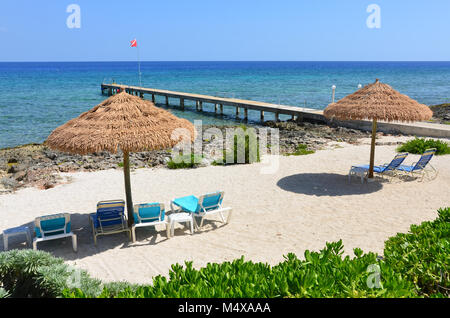 Diver's Pier und geschützten Strand, mit Stroh Sonnenschirme und Liegestühle in Grand Cayman. Stockfoto