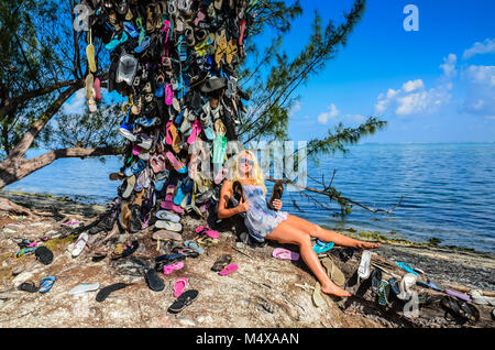 Sonnengebräunte blonde Mädchen liegt an einem Baum in Flip Flops von Touristen in Grand Cayman Island in der Karibik links abgedeckt. Stockfoto