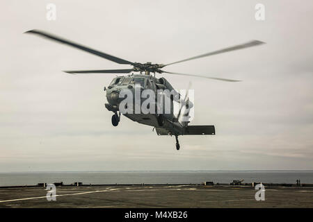 Ein U.S. Navy MH-60S Seahawk Helikopter mit Hubschrauber Meer Combat Squadron 28, schwebt über dem Flight Deck an Bord der Station Landung Schiff USS Oak Hill (LSD 51) Bei Flugbetrieb vor der Küste von North Carolina in den Atlantik, 14.02.2018. Das Oak Hill und die 26 Marine Expeditionary Unit sind an einem Einsatz auf See see- und friedenserhaltende Maßnahmen durchzuführen, sowie die Pflege der Beziehungen zu ausländischen Armeen durch gemeinsame Übungen. (U.S. Marine Corps Foto: Staff Sgt. Dengrier M. Baez) Stockfoto