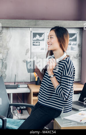 Asiatische Geschäftsfrau eine Kaffee Pause nach der Arbeit mit einem Lächeln im Gesicht, glücklich Büro Lebenskonzept, berufstätige Frau im modernen Büro zu Hause. Stockfoto