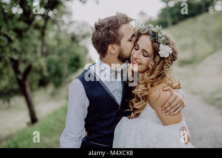 Schöne junge Paare, Bräutigam und Braut mit Blumenkranz außerhalb in der grünen Natur. Ein Mann eine Frau zu küssen. Stockfoto
