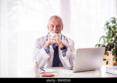 Älterer männlicher Arzt mit Laptop am Schreibtisch sitzen. Stockfoto