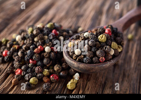 Ansicht von oben in einem hölzernen Löffel voll von schwarzen, roten, gelben, weißen Pfefferkörner auf dunklem Hintergrund. Es isa Haufen von piment Samen hinter sich. Stockfoto