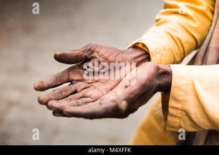 Zerknitterte alte Hände eines Unbekannten, Gelb gekleidet, indische Brahman, die Betteln ist für Geld. Nahaufnahme der Hände mit softfocus Hintergrund. Menschliche Gefühle. Stockfoto