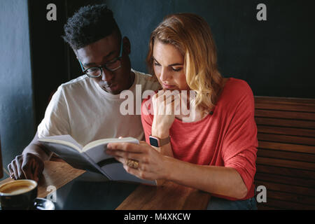 Der Mann und die Frau sitzt an einem Tisch zusammen ein Buch zu lesen. Paar im Coffeeshop ein Buch lesen bei einer Tasse Kaffee auf dem Tisch. Stockfoto