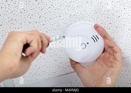 Nahaufnahme von einer Person die Hand mit einem Schraubendreher zu installieren Sie Rauchmelder an der Decke zu Hause Stockfoto