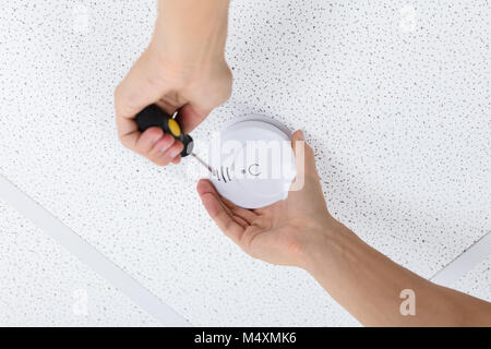Nahaufnahme von einer Person die Hand mit einem Schraubendreher zu installieren Sie Rauchmelder an der Decke zu Hause Stockfoto
