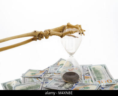 Skelett Finger holding Sand - Glas auf Dollar platziert. Konzept der Zeit - Geld und Tod. Stockfoto