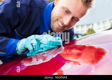 Junge Glücklich männlichen Arbeitnehmers rotes Auto mit Lappen reinigen Stockfoto