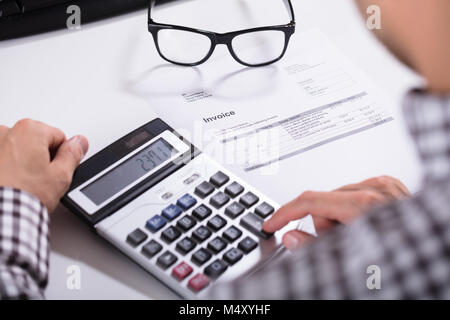 Nahaufnahme der Geschäftsmann Hände Berechnung Rechnung mit Taschenrechner mit Brillen auf Schreibtisch Stockfoto
