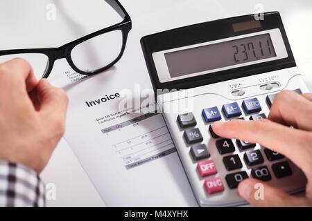 Nahaufnahme der Geschäftsmann Hände Berechnung Rechnung mit Taschenrechner mit Brillen auf Schreibtisch Stockfoto