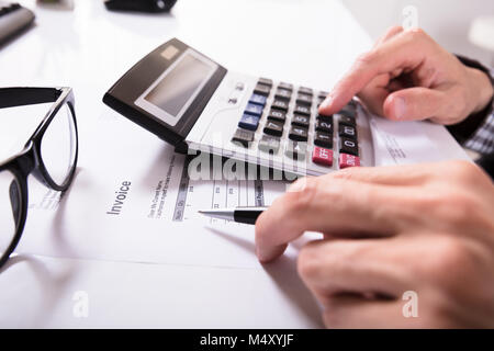 Nahaufnahme der Geschäftsmann Hände Berechnung Rechnung mit Taschenrechner mit Brillen auf Schreibtisch Stockfoto