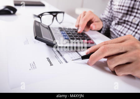 Nahaufnahme der Geschäftsmann Hände Berechnung Rechnung mit Taschenrechner mit Brillen auf Schreibtisch Stockfoto