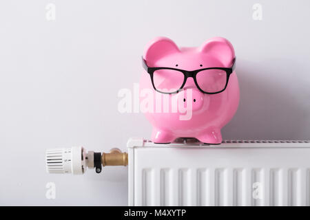 Nahaufnahme der Thermostat und das Sparschwein mit Brillen am Kühler gegen Weiße Wand Stockfoto