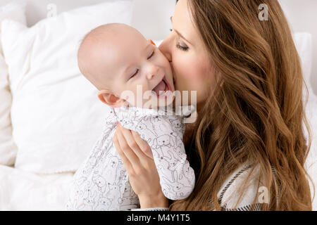 Glückliche Mutter küssen ihr adorable Baby Sohn. Glückliche Familie. Mutter und das Neugeborene spielen im Kindergarten portrait. Stockfoto