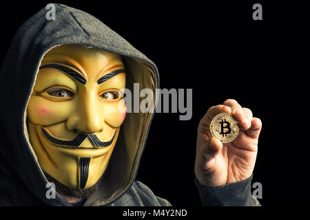 Mailand, Italien, Februar 2018: Hacker halten Golden bitcoin Münze und Verschleiß anonymus Maske. Editorial Foto. Stockfoto