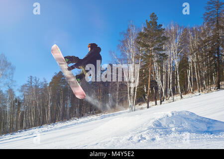 Portrait des jungen Mannes, Durchführung von Snowboard stunt fliegen hoch in der Luft gegen den klaren blauen Himmel über die Piste, kopieren Raum Stockfoto