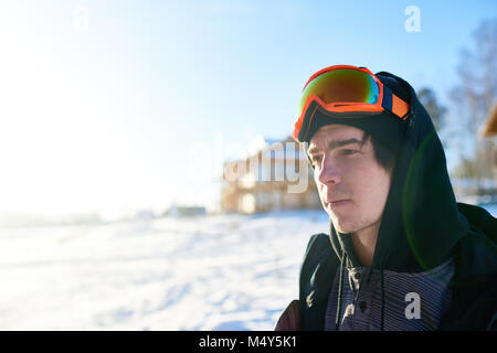 Portrait von hübscher junger Snowboarder weg schauen genießen Sie sonnige Sommer Tag im Skigebiet mit Chalets aus Holz im Hintergrund, kopieren Raum Stockfoto